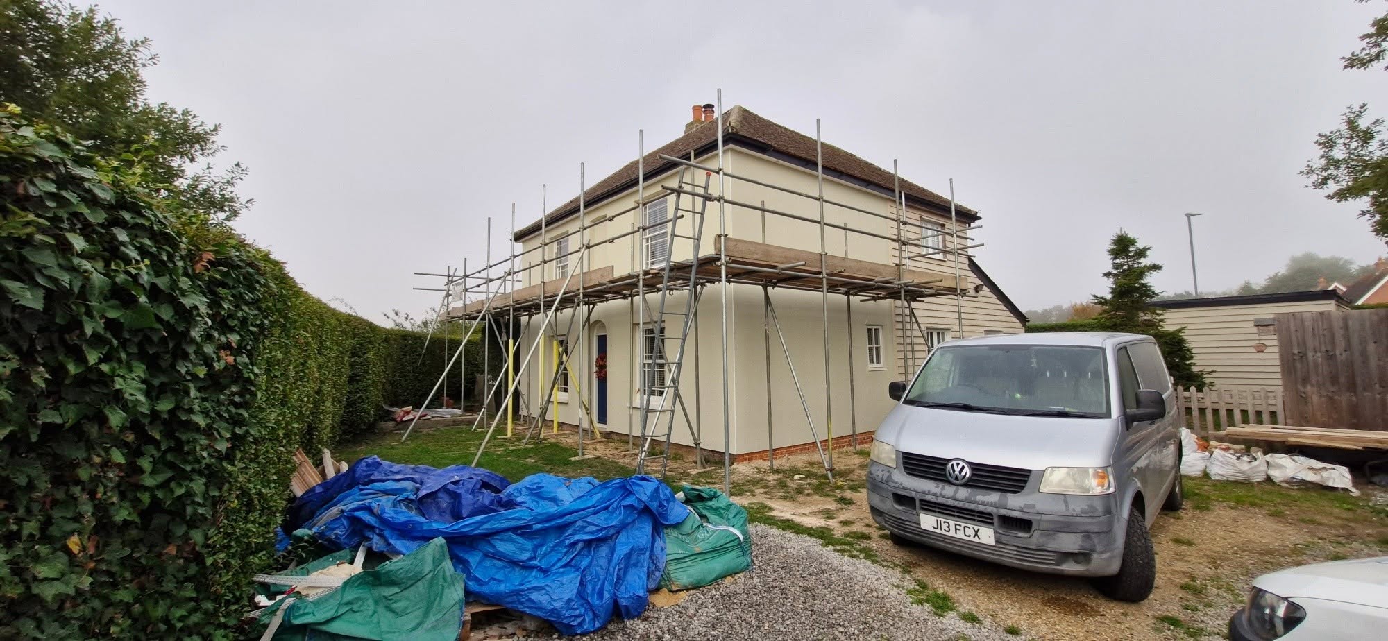 Cream-rendered house under scaffolding during an exterior job