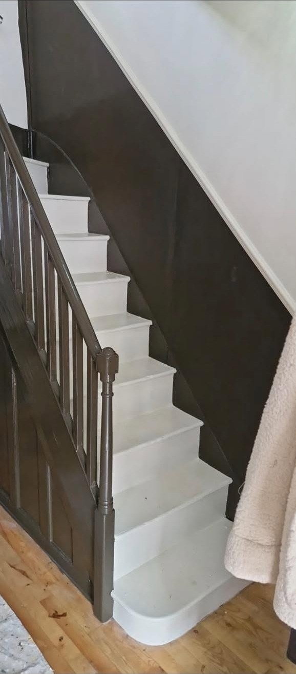 Staircase with white treads, grey handrail and spindles against a dark feature wall