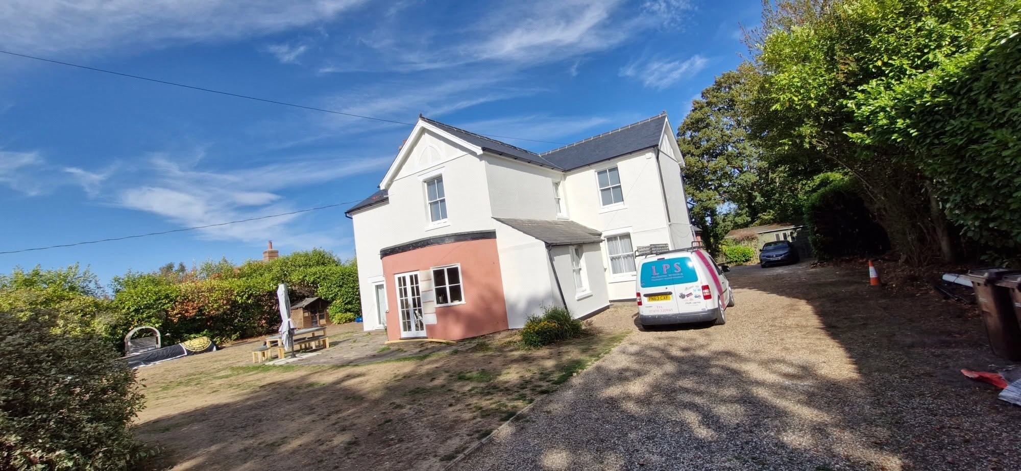 White-rendered house with a pink-washed wing and the LPS van on the drive