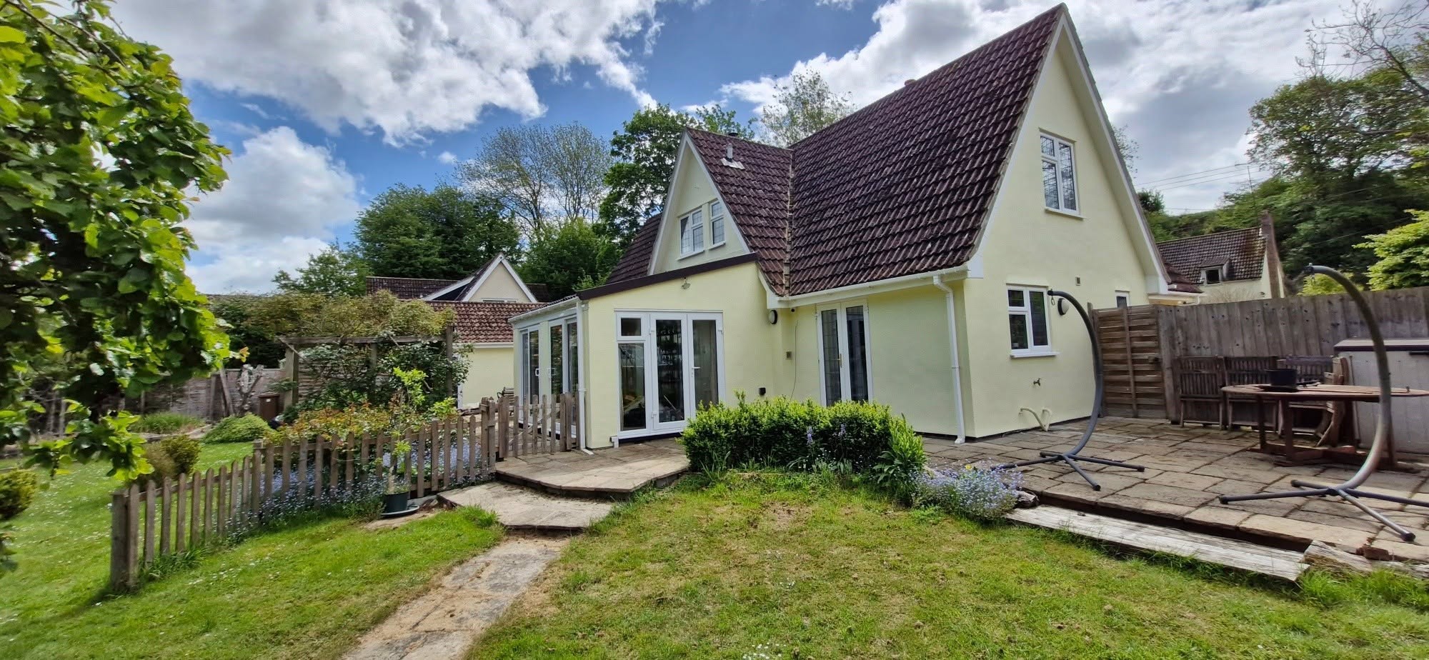 Cream chalet house with a conservatory and a lawned garden